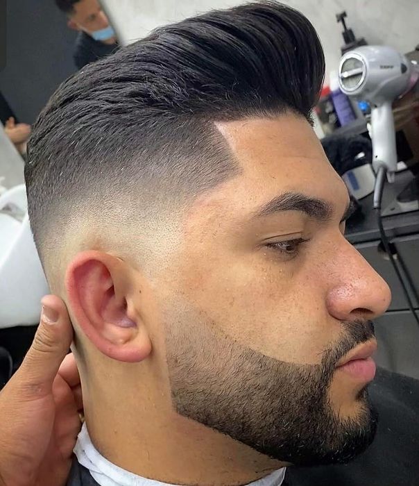 Skin fade with a combed-back top and beard line-up